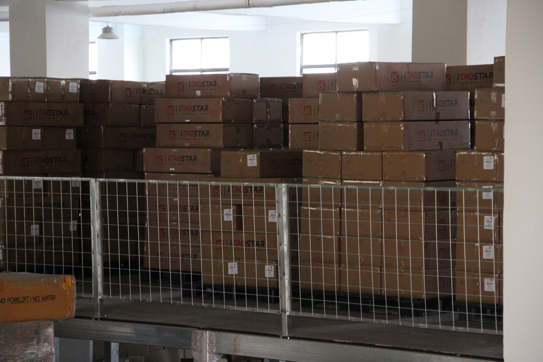Stacked cartons behind a cage partition in the factory.