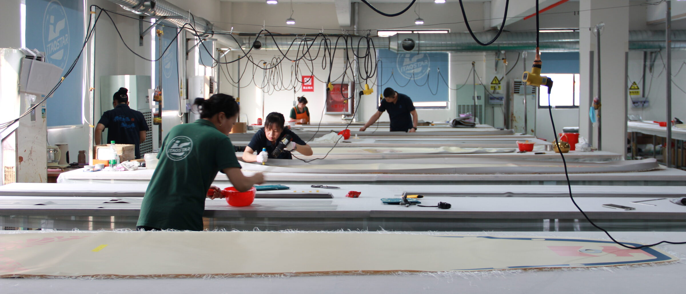 Production floor with several paddle boards in progress and two operators working.